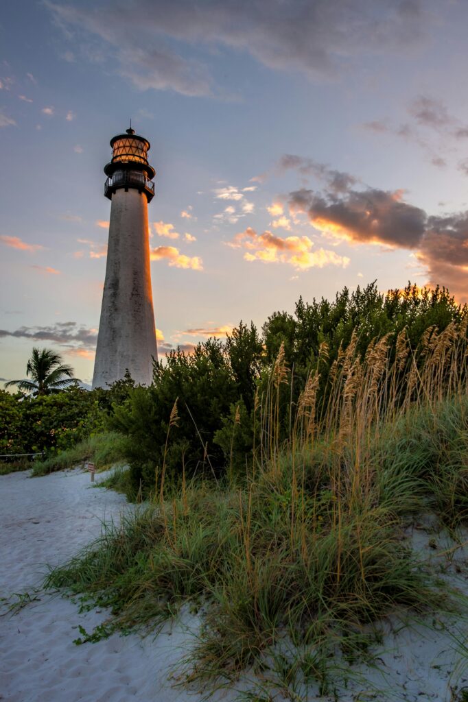 Find Your School District Cape Florida Lighthouse surrounded by beach grass at sunset, vibrant sky.